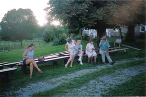 A shot of the women, sitting on benches, waiting to clean the tables under the canopy.